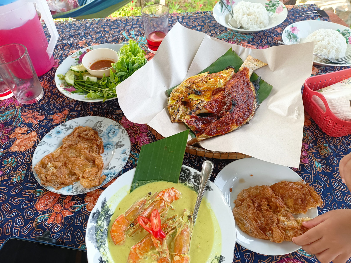 Grilled fish, prawn curry, omelettes, rice and vegetables on a patterned table.