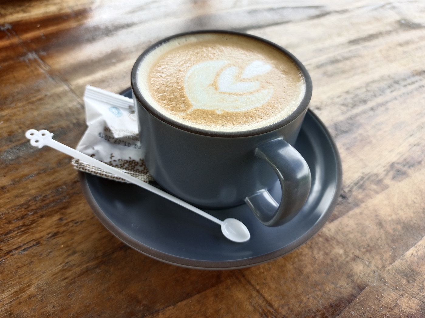 A hot coffee with leaf-shaped foam art on a wooden table.